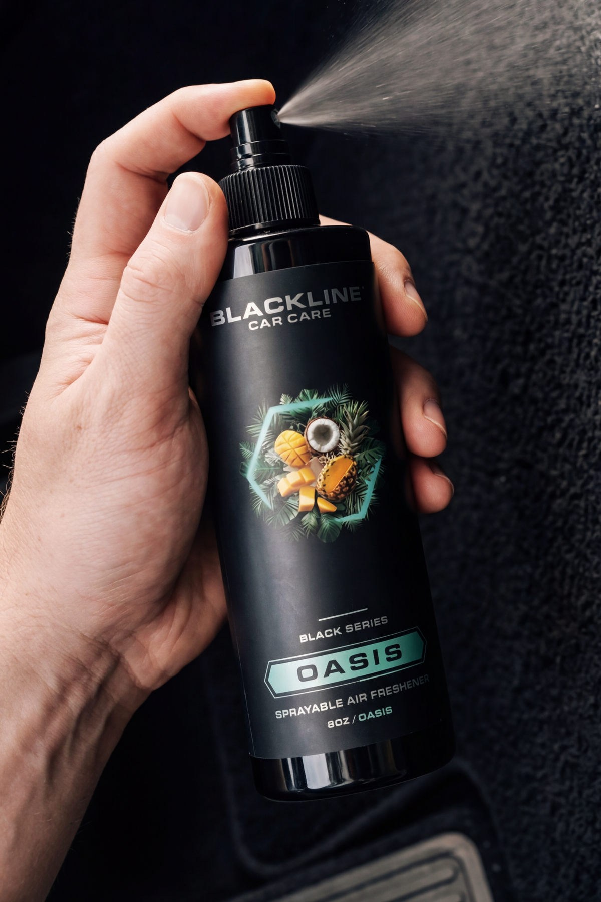 Hand spraying Blackline Oasis air freshener with visible mist in dark setting.