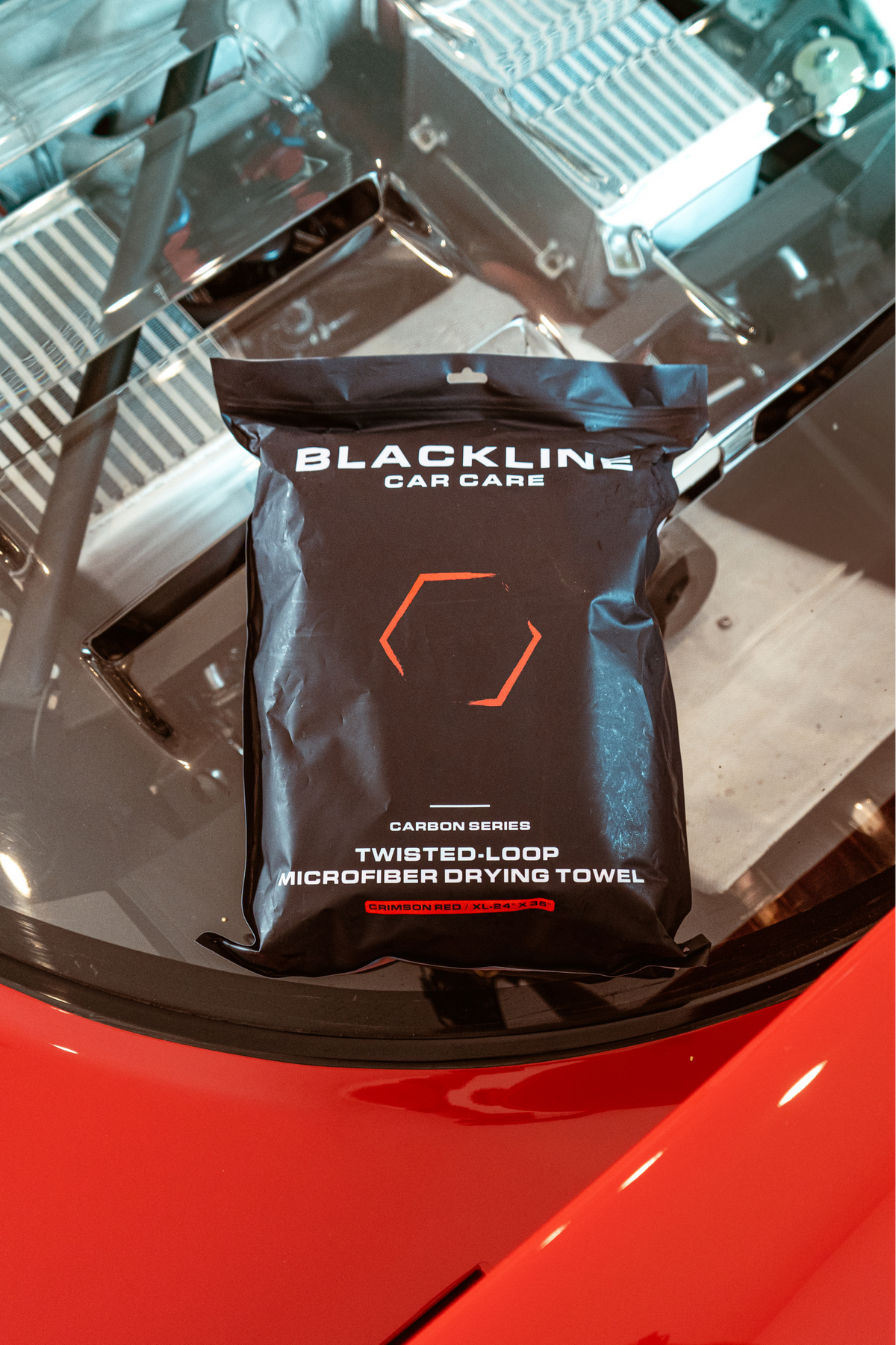 Sealed retail packaging of the Blackline twisted-loop microfiber drying towel resting on the glossy black hood of a car.