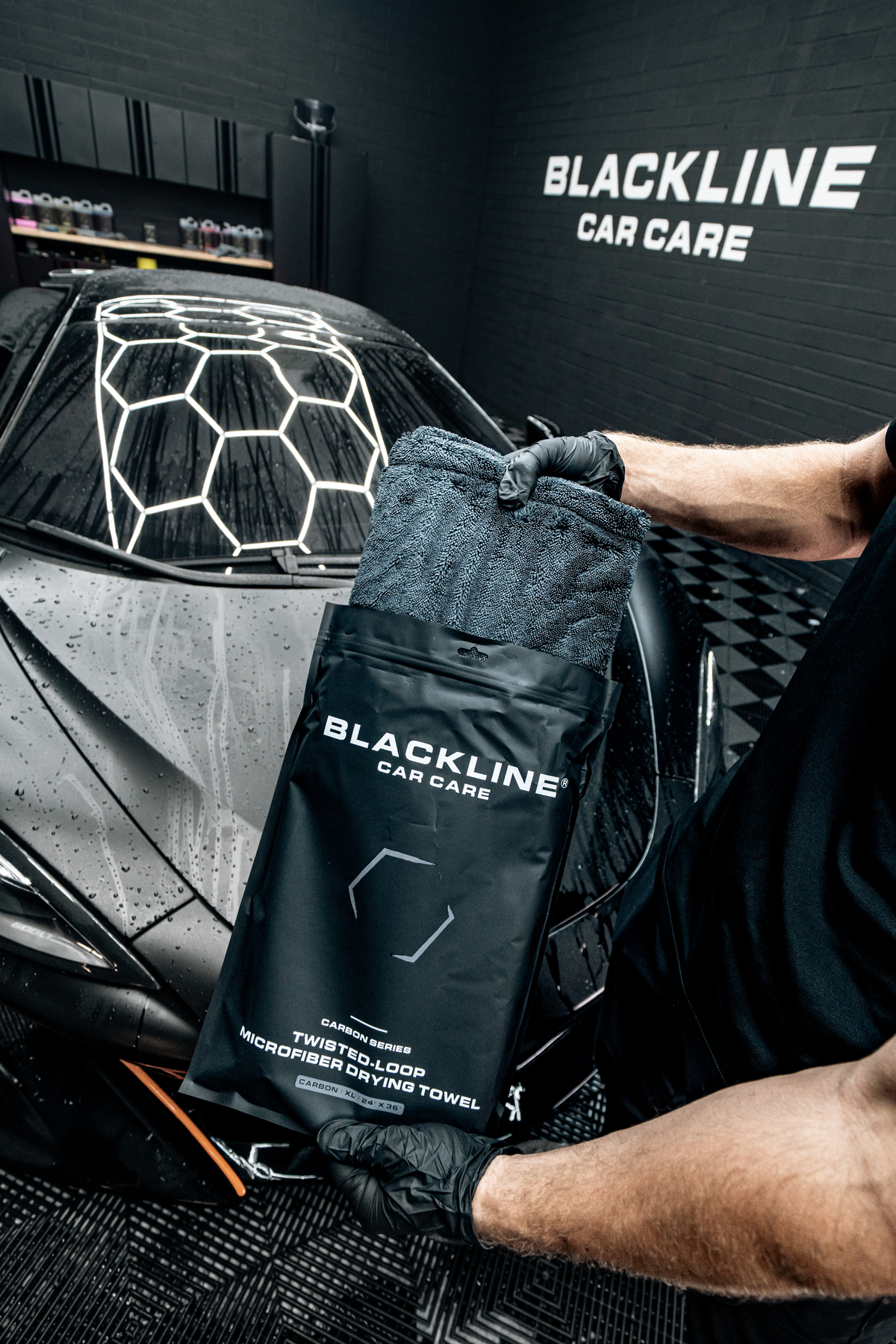 A person inside a Blackline Car Care detailing bay unboxing the twisted-loop drying towel from its black storage pouch.