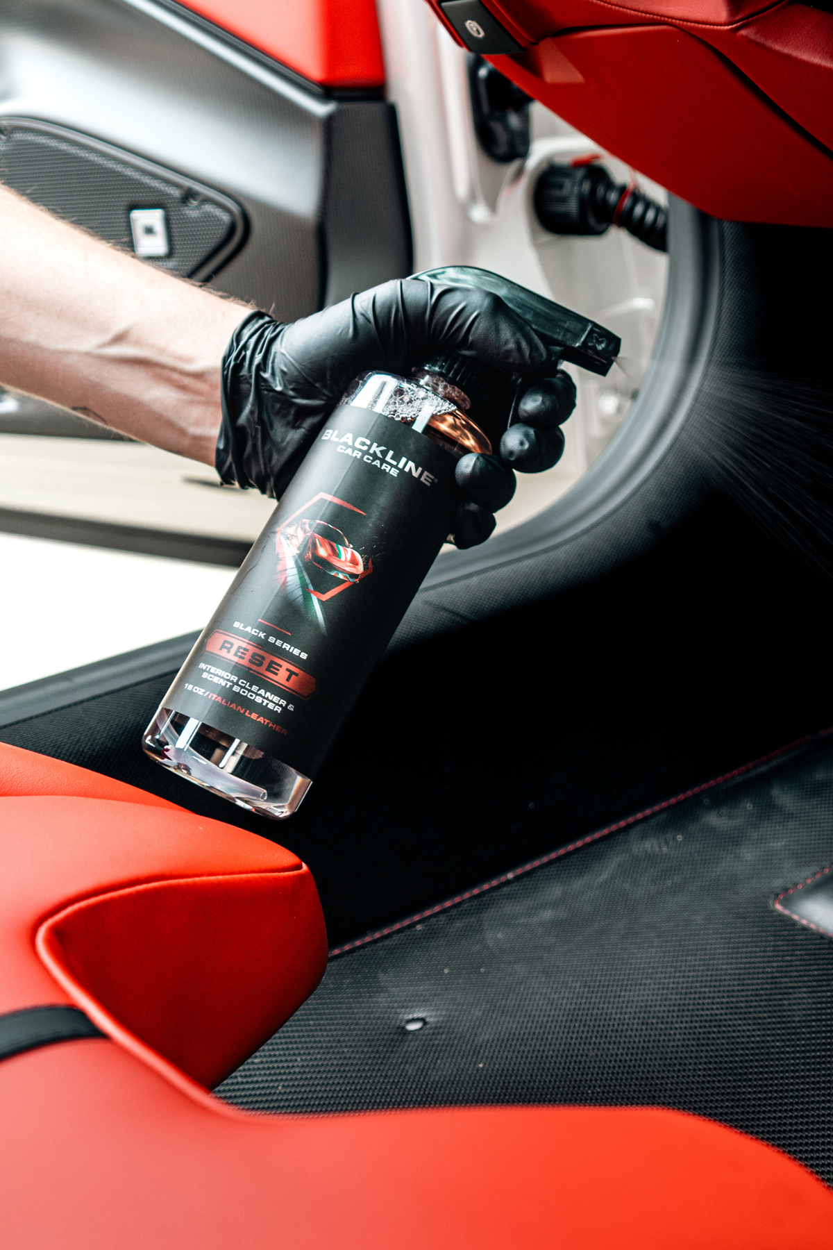 Hand spraying Blackline Reset Italian Leather interior cleaner onto a car interior surface.
