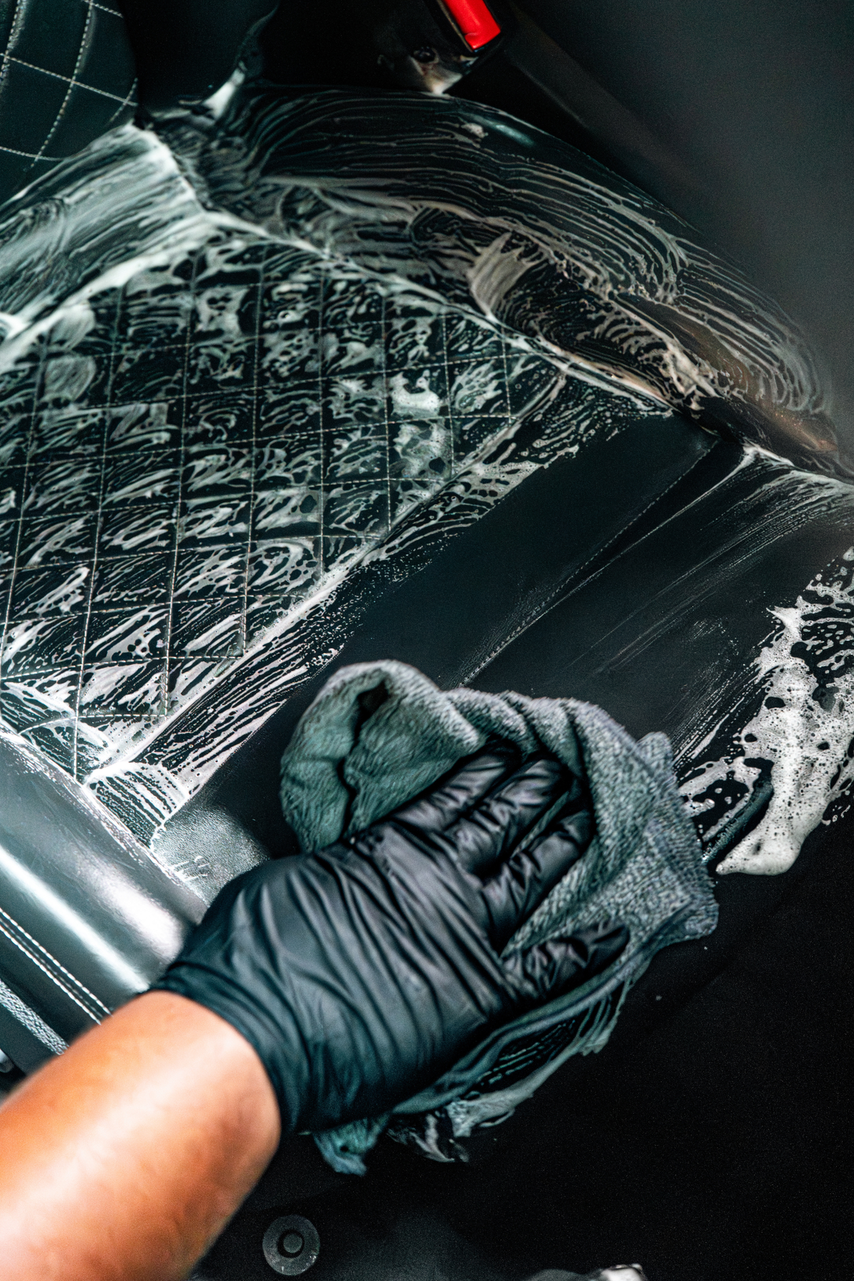 Black-gloved hand using a microfiber towel to wipe down a luxury vehicle interior with Blackline Gentle APC.