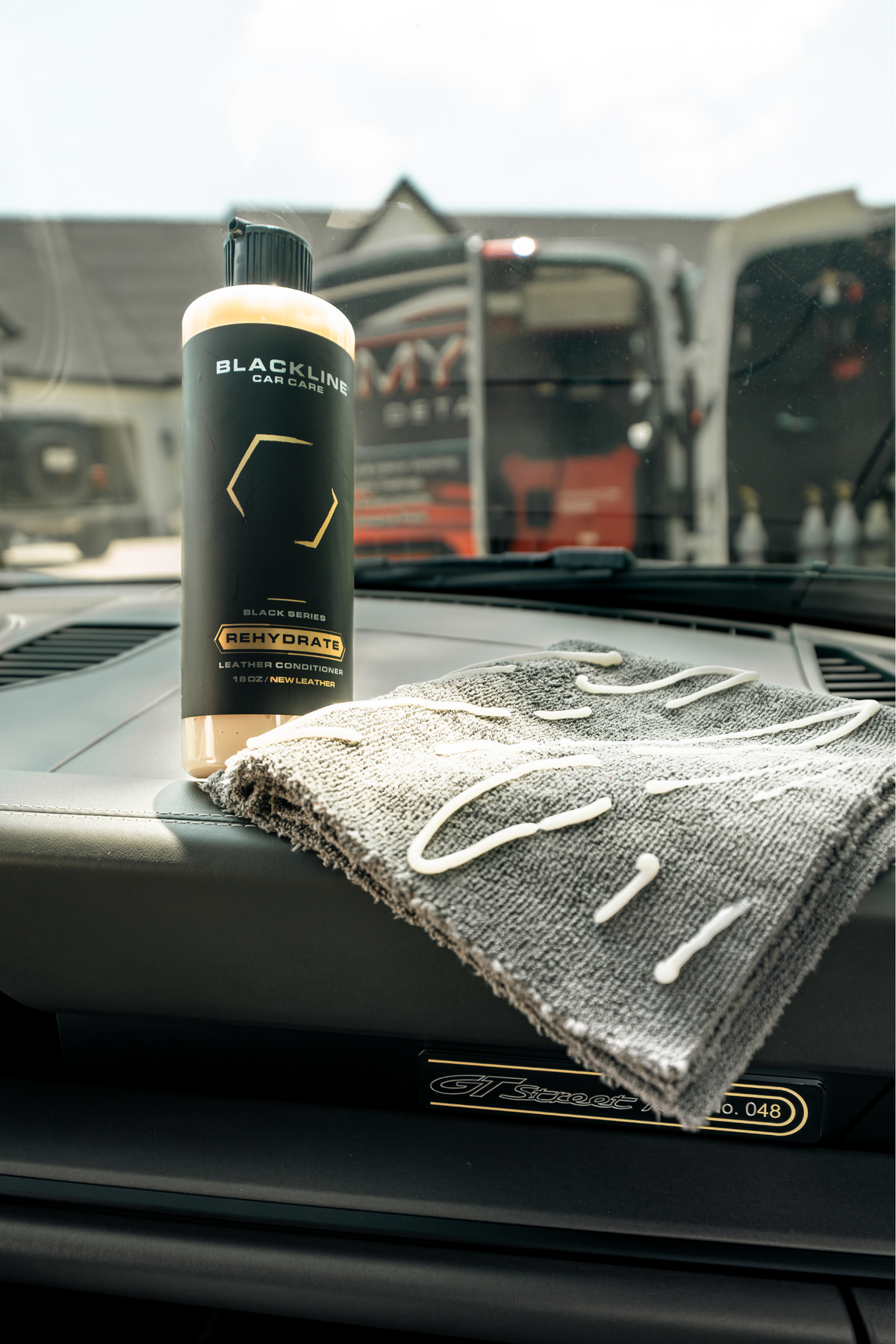 Hand applying Blackline Rehydrate Leather Conditioner to a vehicle's leather seat.