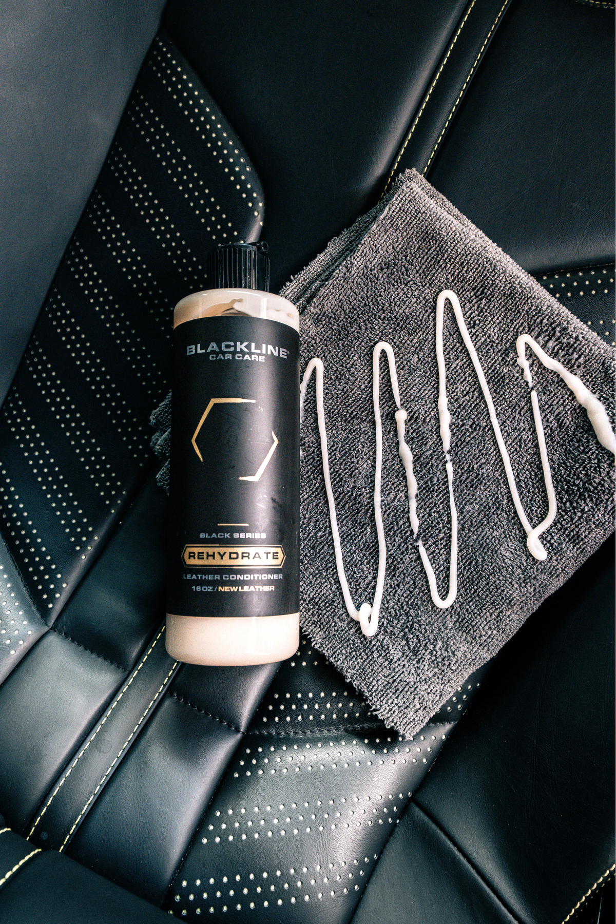 Hand holding the Blackline Gentle APC bottle in front of a leather seat with a microfiber towel.