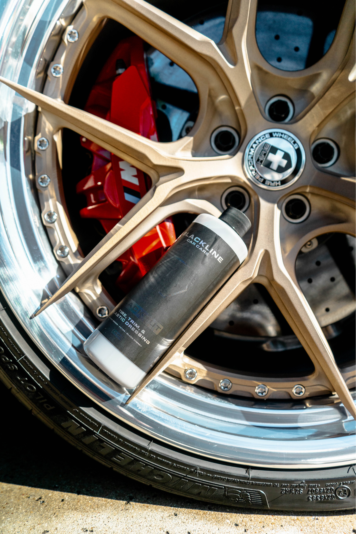 Wheel with bronze rim and red brake caliper, freshly dressed with Blackline Blackout tire dressing.
