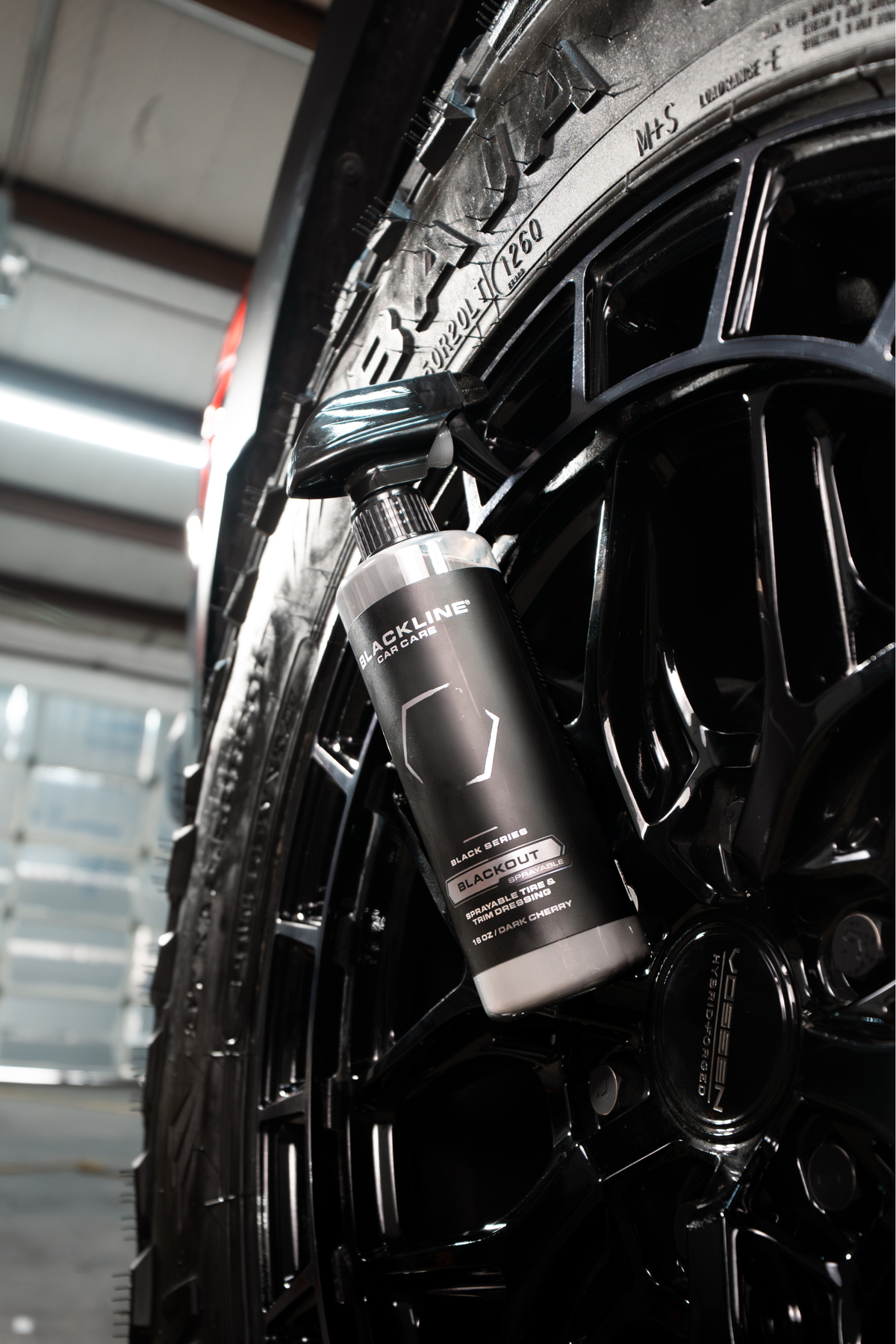 Black Blackline Blackout bottle leaning against a glossy black wheel.
