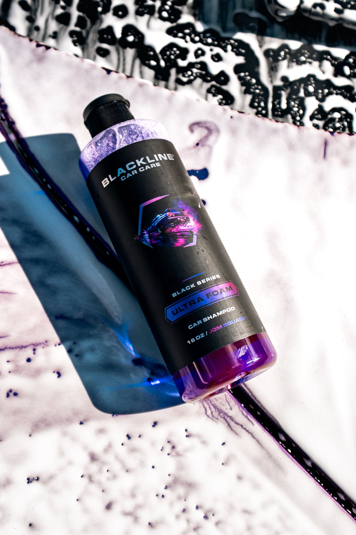 Lifestyle close-up of the Blackline Ultra Foam JDM Squash bottle resting on a vehicle covered in purple-tinted foam during a wash.